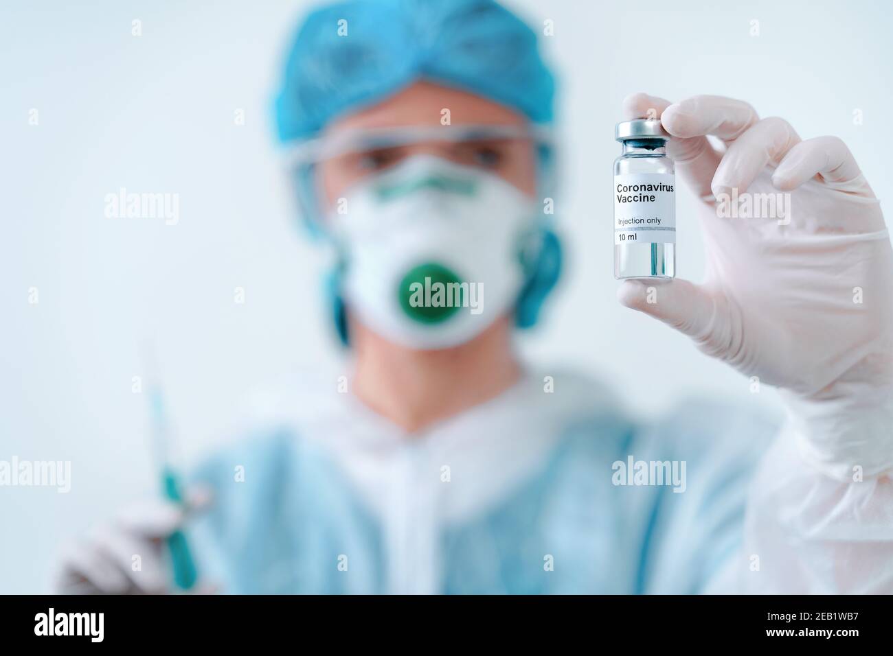 Nurse in protective suit and mask holds an injection syringe and vaccine. Biological hazard. Stock Photo