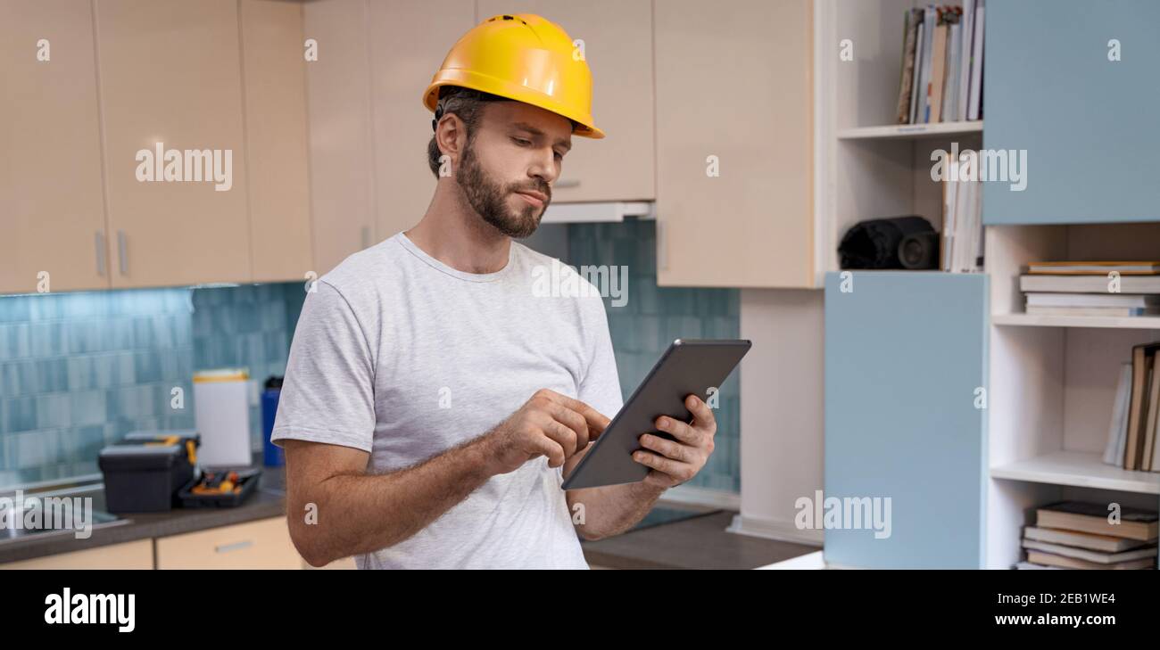 Builder in helmet working with tablet on kitchen background Stock Photo