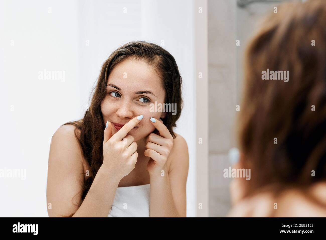 Young woman  looking and squeeze  acne on a face in front of the mirror. Ugly problem skin girl, teen girl having pimples. Skin care. Beauty Stock Photo