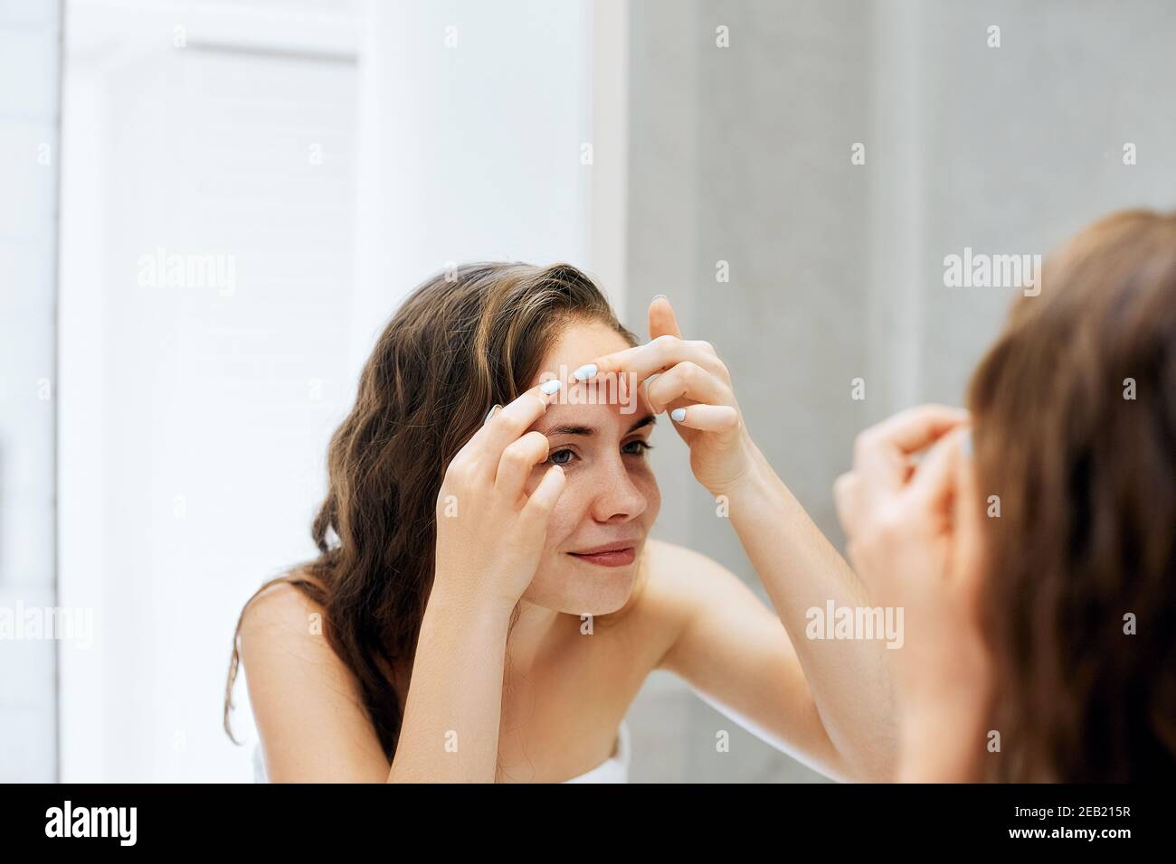 Young woman  looking and squeeze  acne on a face in front of the mirror. Ugly problem skin girl, teen girl having pimples. Skin care. Beauty Stock Photo