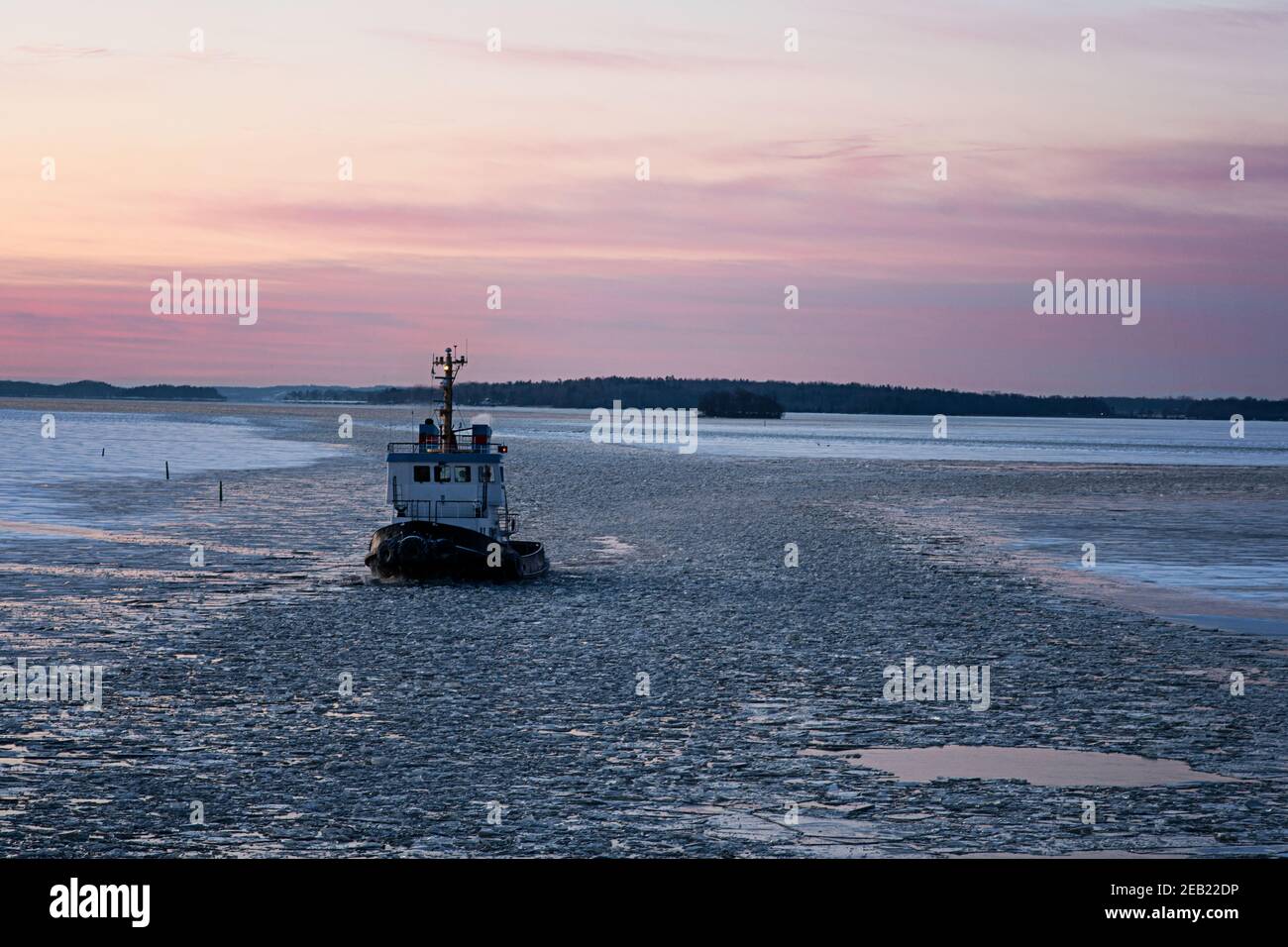 Icebreaker ship breaking through the ice during a beautiful sunset, proving safe waterways for other boats, ships and vessels during winter season. Stock Photo