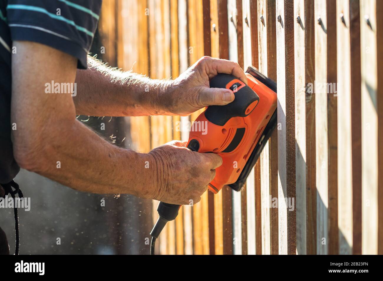 Sanding wood. Close-up vibrating sander in hands. Grinding and repairing wooden fence Stock Photo