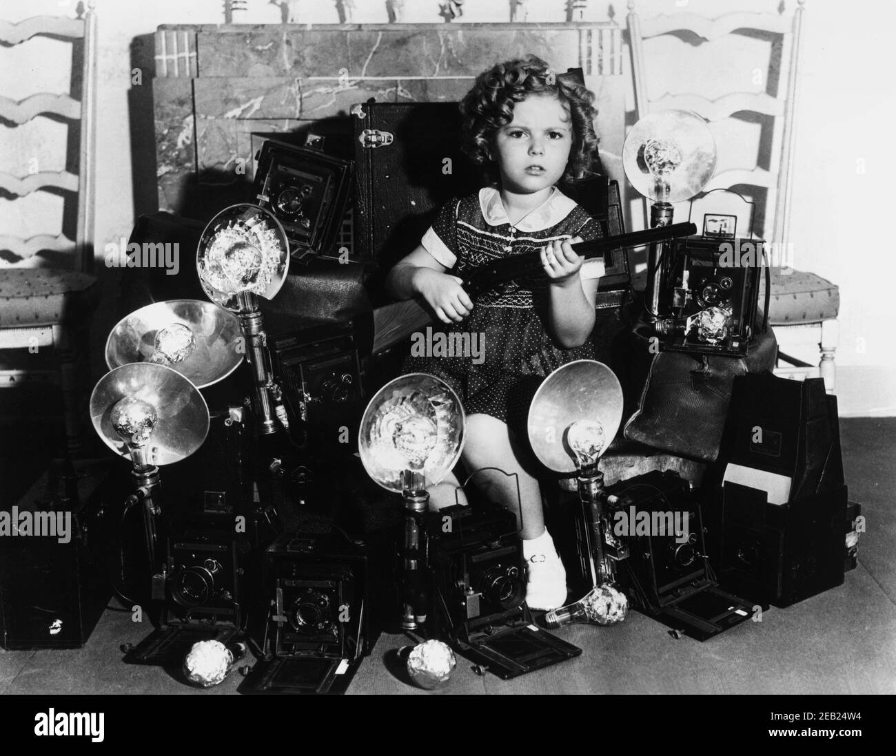 1935 ca, USA   : The child actress  SHIRLEY TEMPLE ( 1928 -  2014 ) about the photographers  , Fox movie pubblicity still   - MOVIE - FILM - CINEMA - portrait - ritratto  - boccoli - riccioli - curls   - bambino prodigio  - macchina fotografica - photo camera - rifle gun - fucile - paparazzi - paparazzo  ----  Archivio GBB Stock Photo