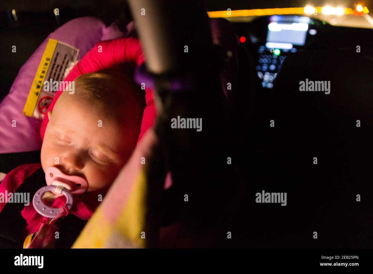 Five-month-old baby asleep in a car seat during a night drive. Stock Photo