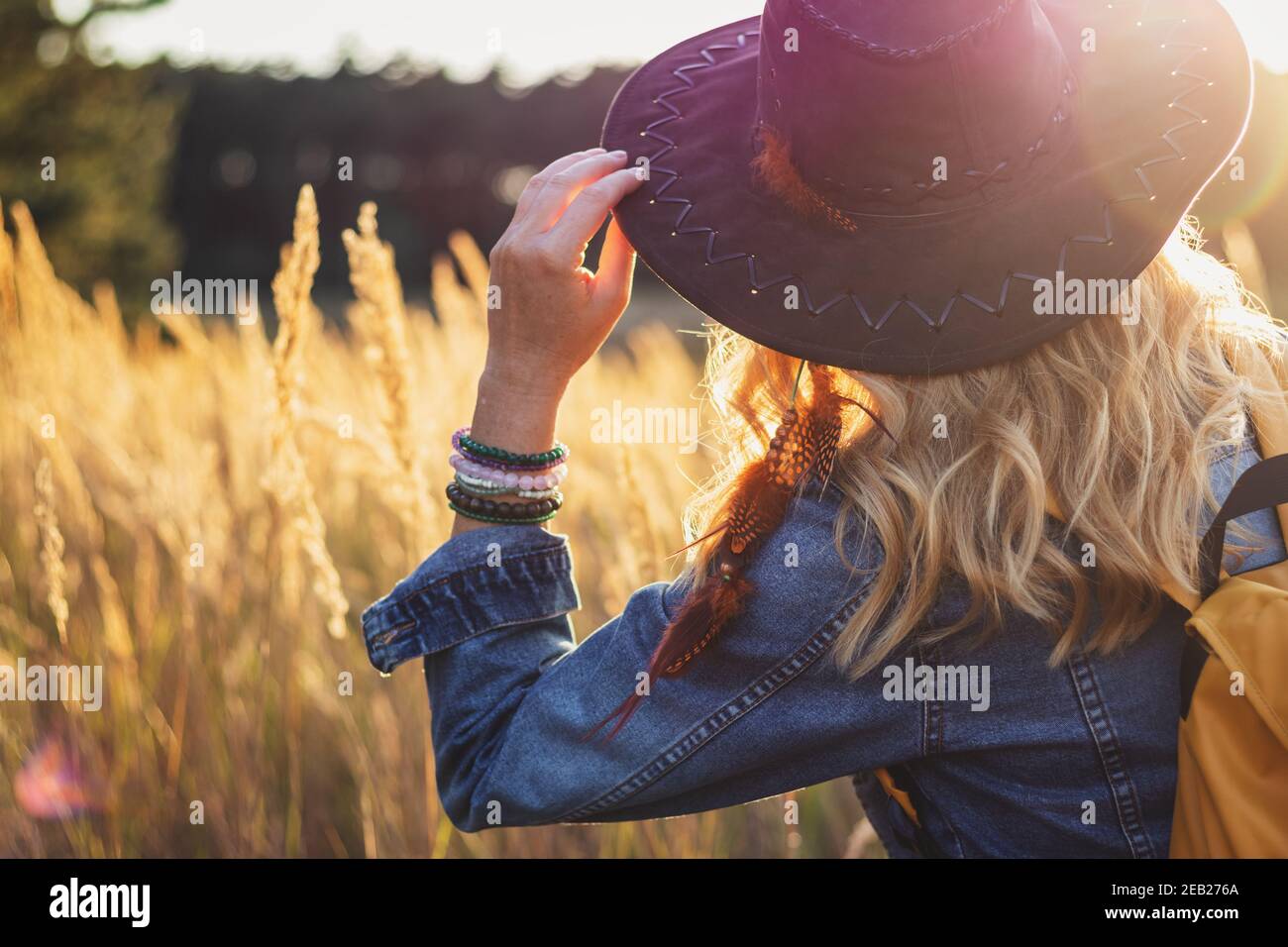 Blond hair woman with hat and denim jacket enjoying sunset outdoors Stock Photo