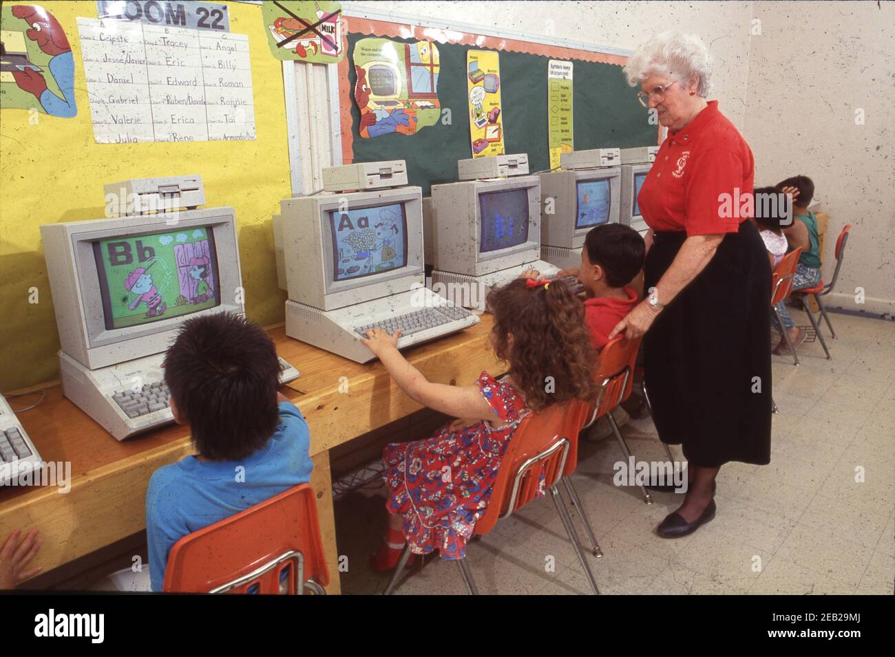 San Antonio, Texas USA: Gray-haired teacher supervises Hispanic kindergarten students in computer lab at elementary school.  Model Release EV-08-11. ©1991 Bob Daemmrich  BAD3384D Stock Photo