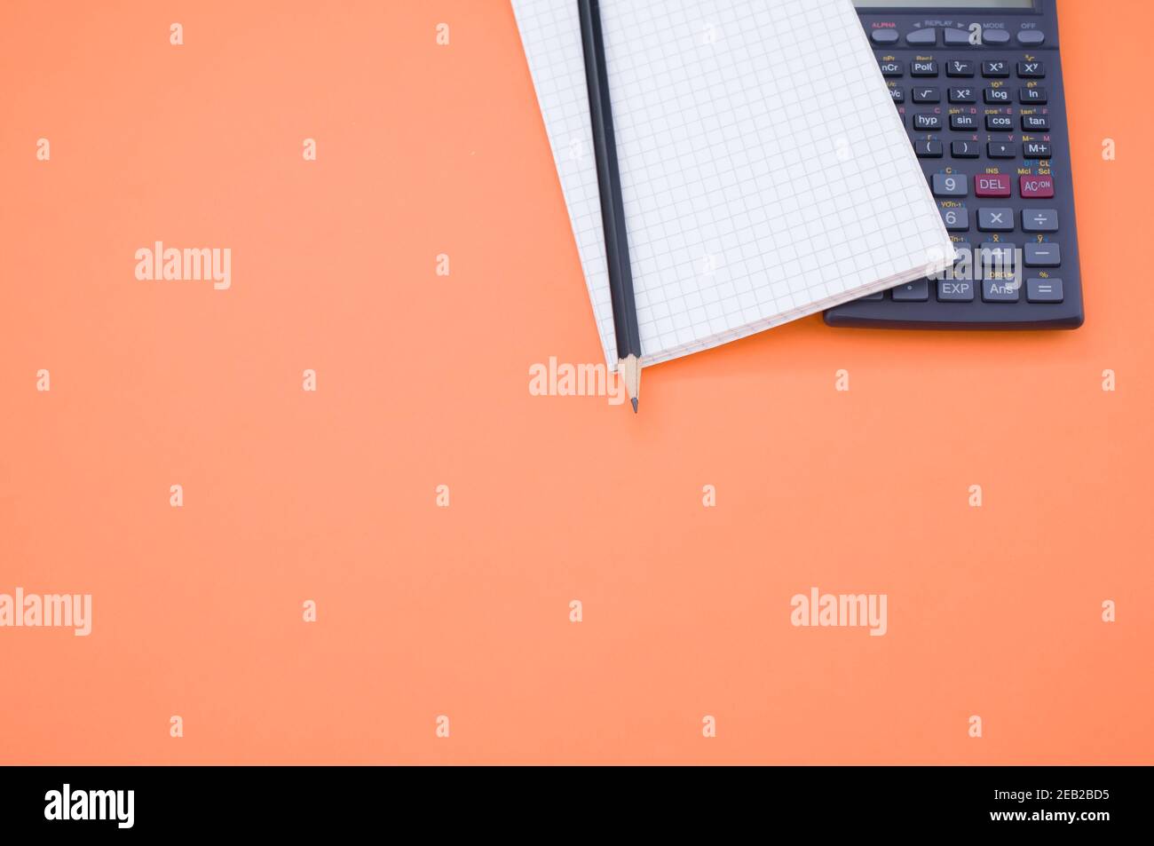 A scientific calculator, notepad and pencil on orange background with