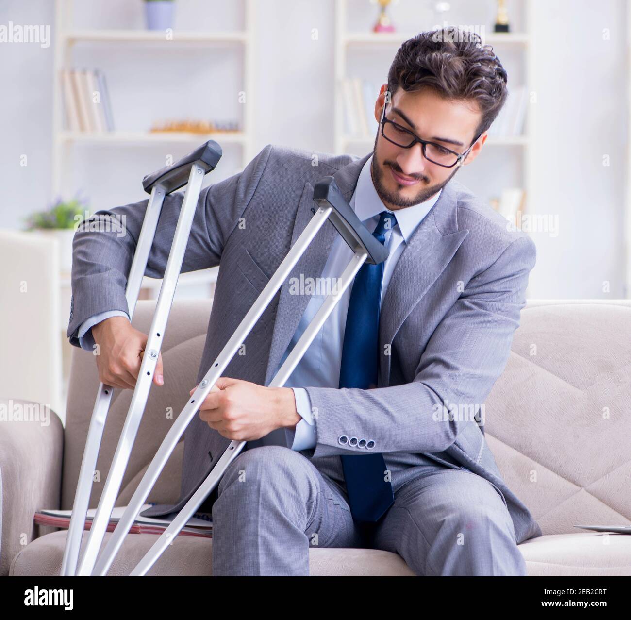 The businessman with crutches and broken leg at home working Stock
