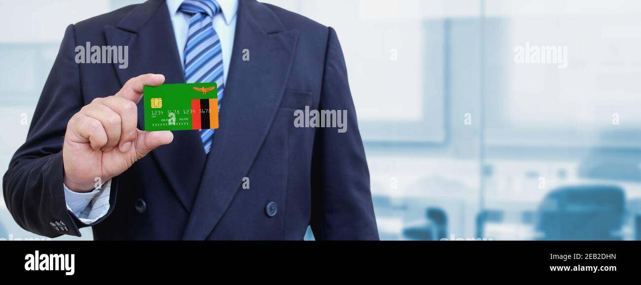 Cropped image of businessman holding plastic credit card with printed flag of Zambia. Background blurred. Stock Photo