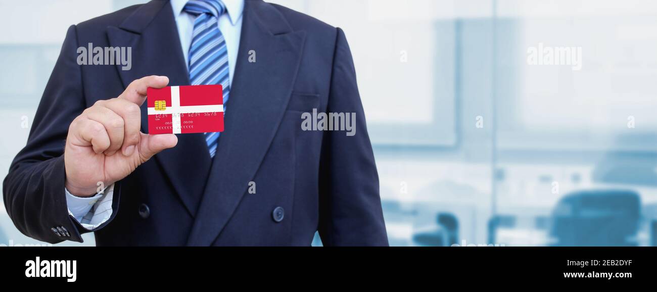 Cropped image of businessman holding plastic credit card with printed flag of Denmark. Background blurred. Stock Photo