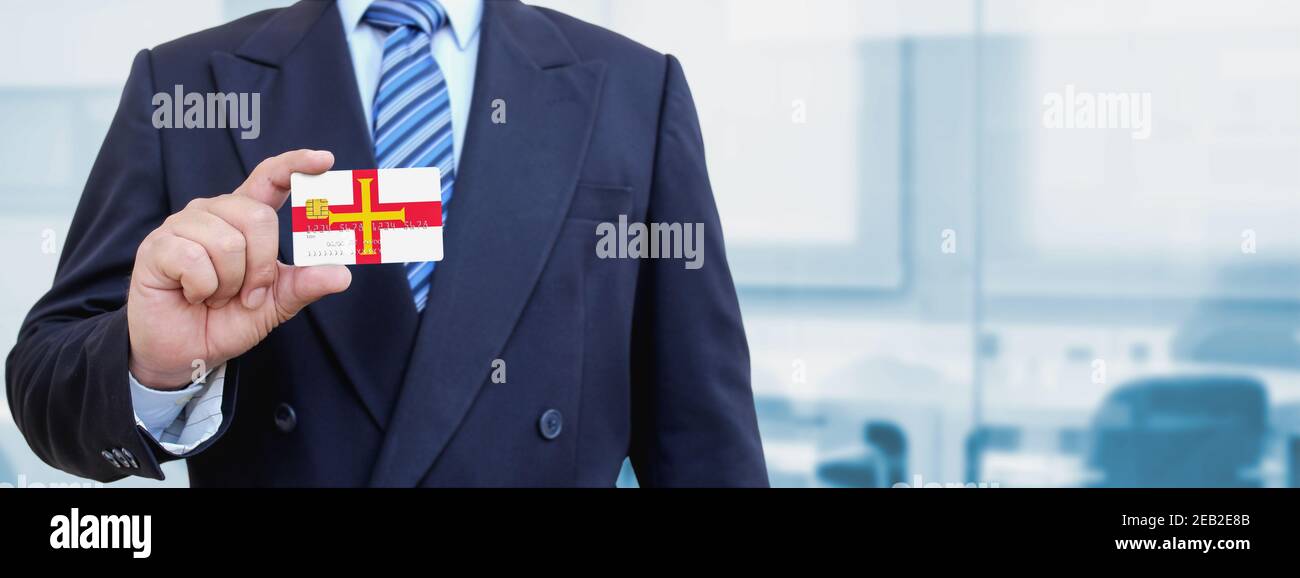 Cropped image of businessman holding plastic credit card with printed flag of Guernsey. Background blurred. Stock Photo