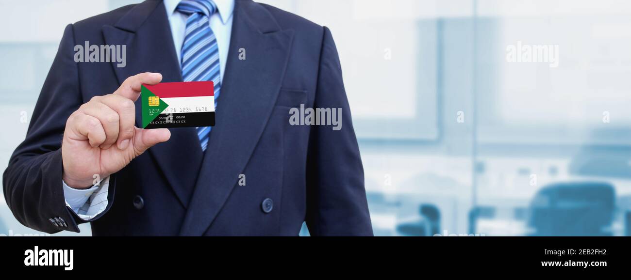 Cropped image of businessman holding plastic credit card with printed flag of Sudan. Background blurred. Stock Photo