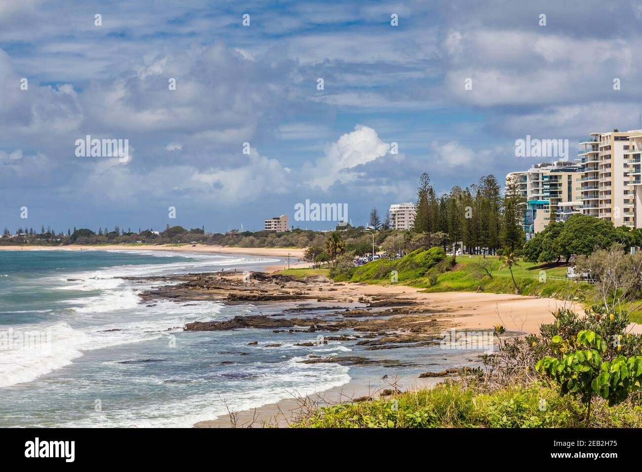 View along Mooloolaba Beach, Queensland, Australia, showing apartments surrounded with greenery, under a cloudy sky. Stock Photo