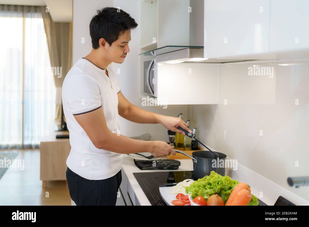 Asian man are using a ladle to thicken vegetable soup in a pot at the home kitchen. Stock Photo