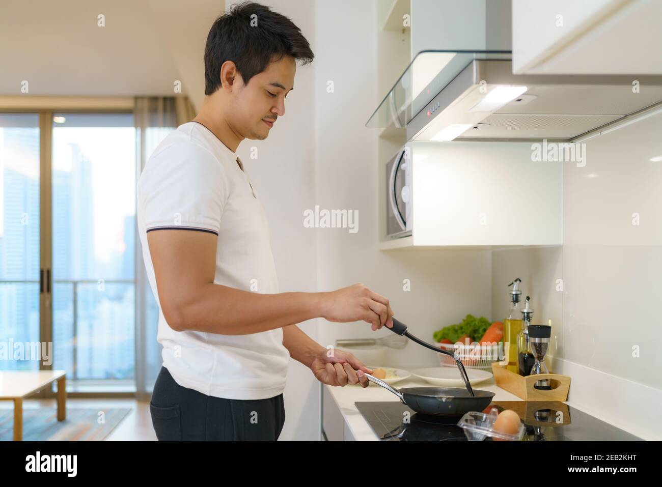 Asian man are cooking American breakfast by frying a fried egg in  pan in their kitchen at home. Stock Photo