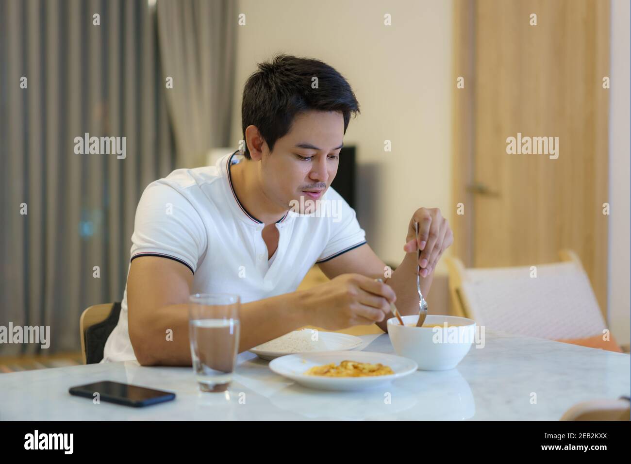 An Asian man is eating dinner alone at the dining table at night at