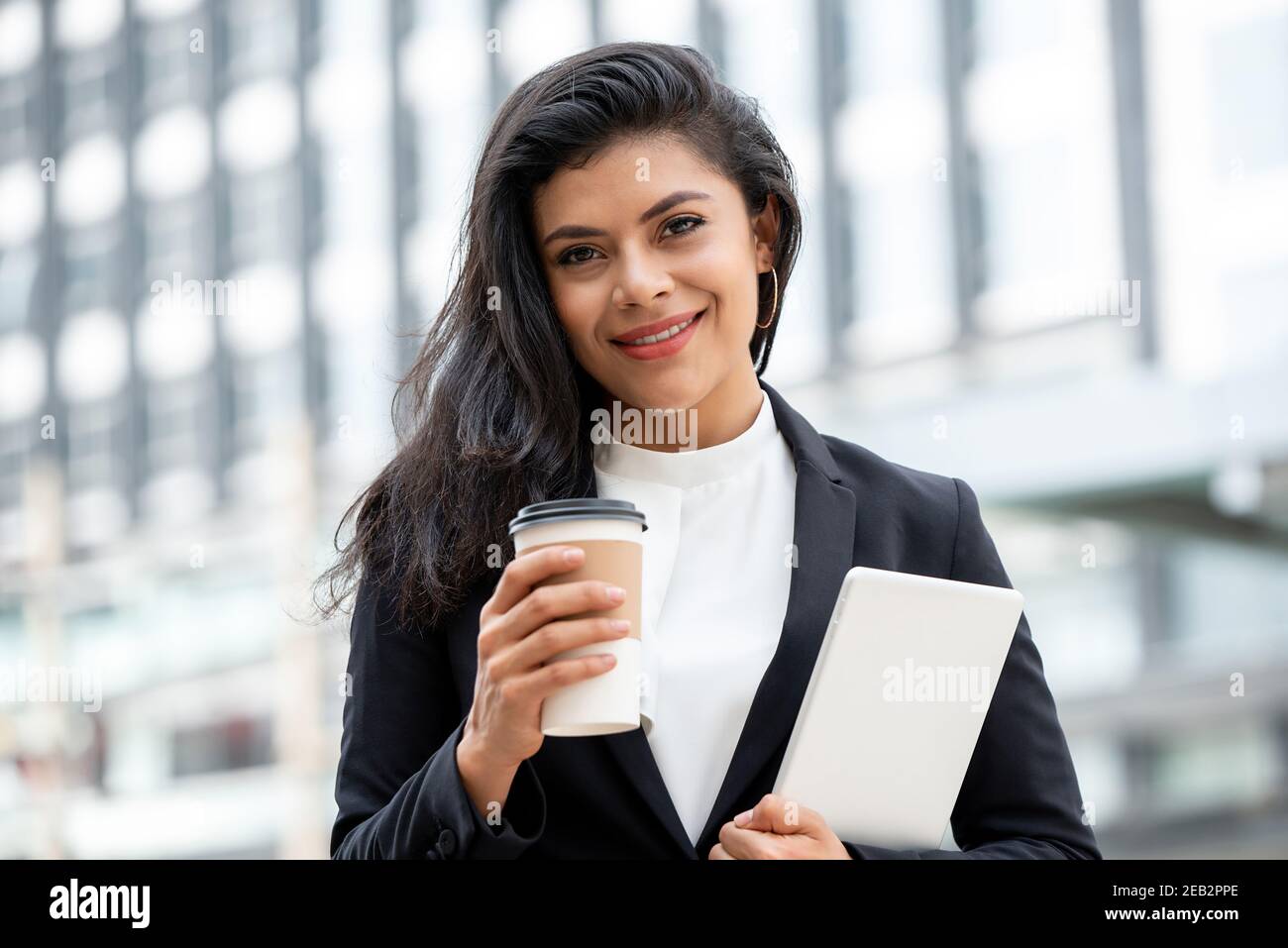 Beautiful smiling Latino businesswoman holding coffee cup and tablet computer outdoors in the city Stock Photo