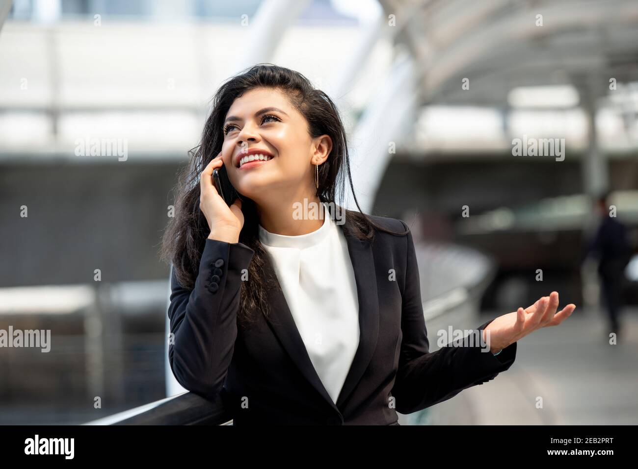 Happy young Hispanic businesswoman talking on mobile phone outdoors in the city Stock Photo