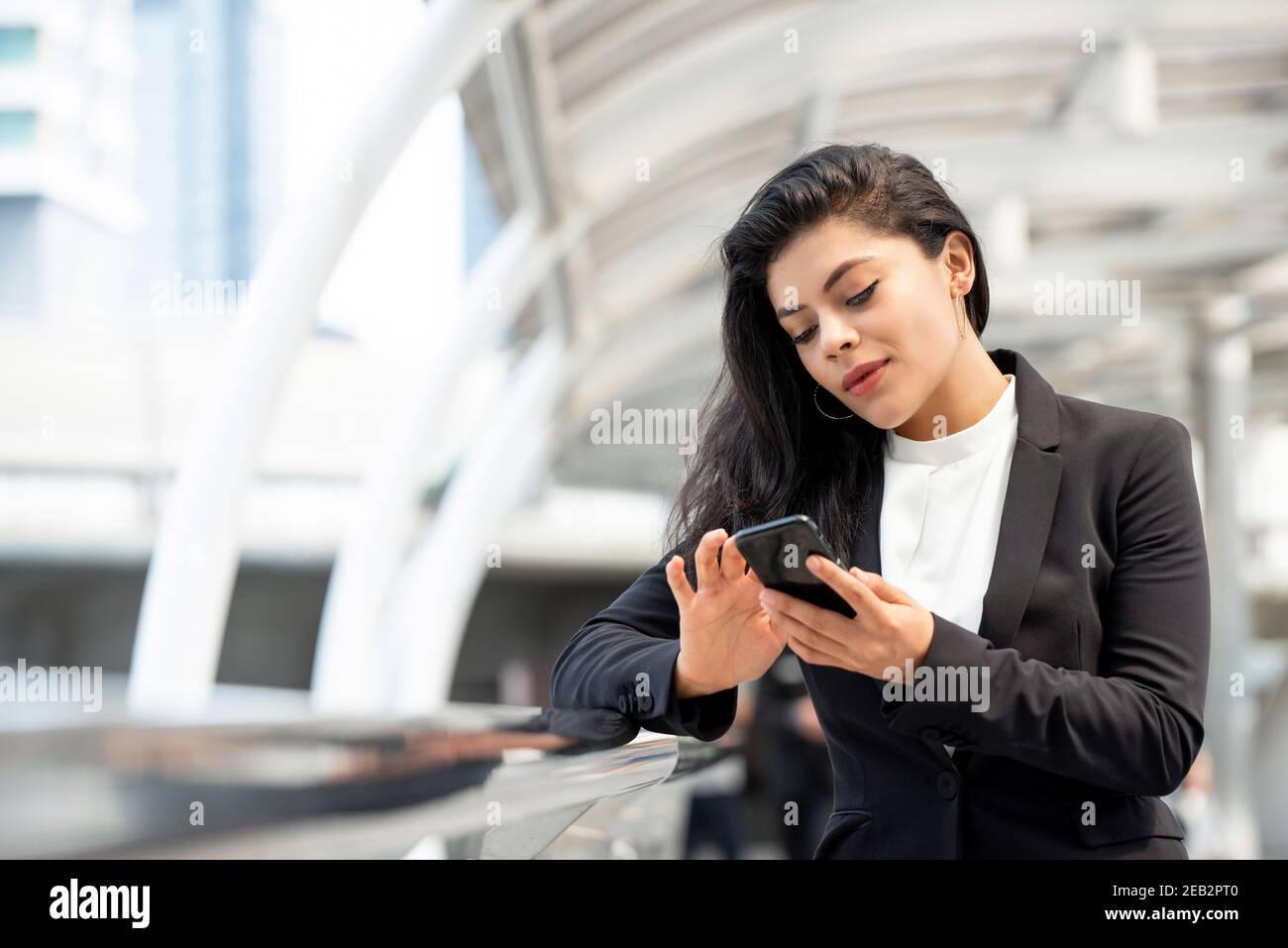 Young beautiful Latin businesswoman using smartphone outdoors in the city Stock Photo
