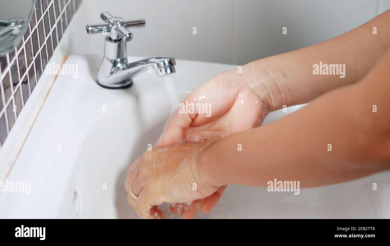 Closeup young woman hands using soap and washing hands under the water ...