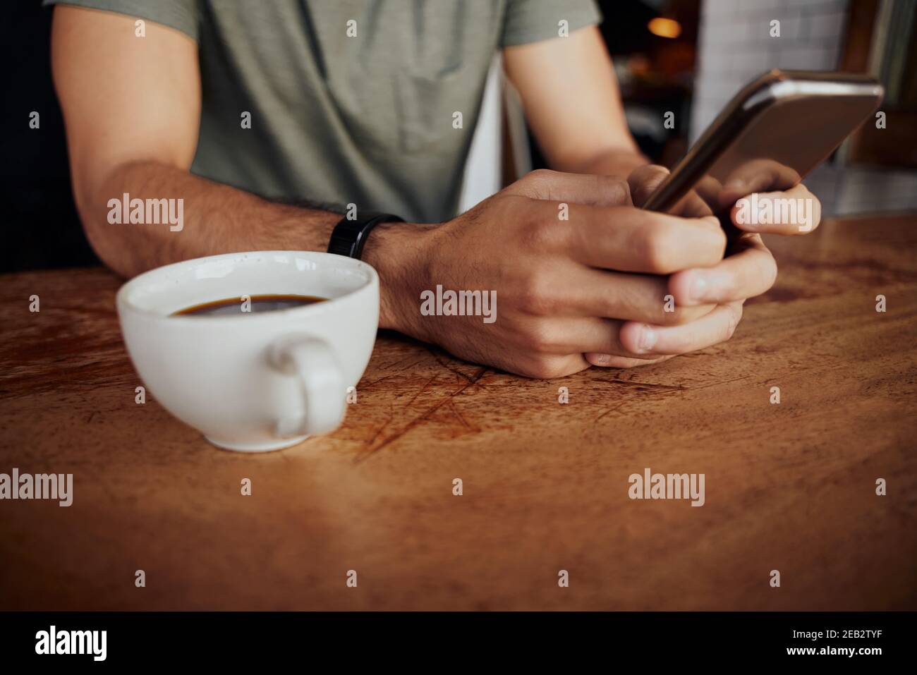 Closeup of male hands holding phone with coffee mug on side while sitting in cafe Stock Photo