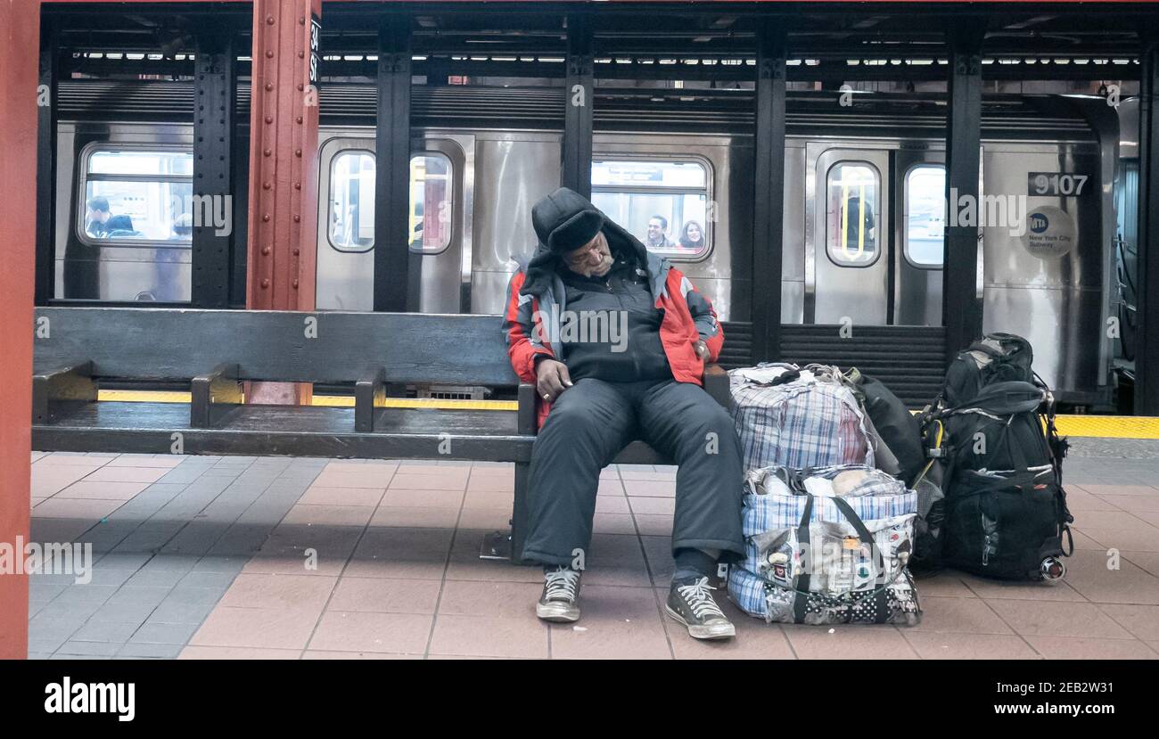 An apparent homeless man sleeps in the New York City subway with his possessions. Stock Photo