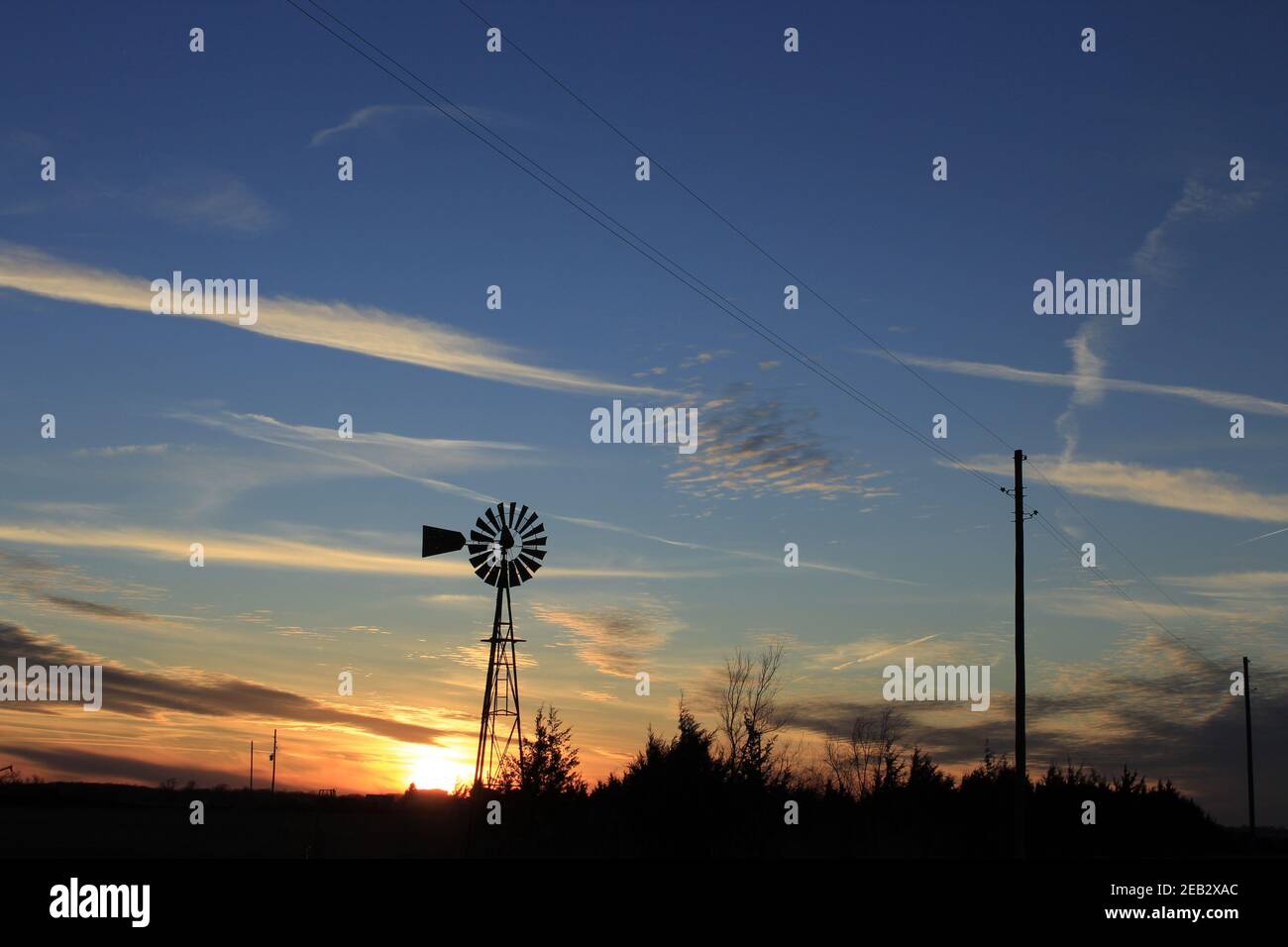 Kansas Sunset with a colorful sky and cloud's with a Windmill and tree silhouette's  out in the country that's bright. Stock Photo