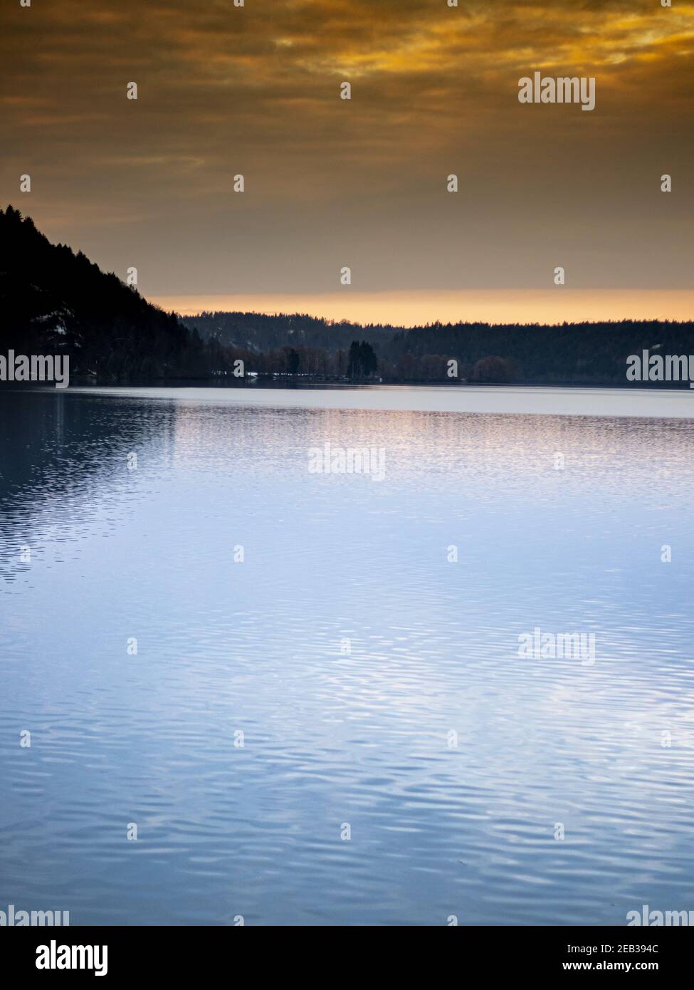 Vertical shot of a beautiful sunset captured in a lake surrounded by ...