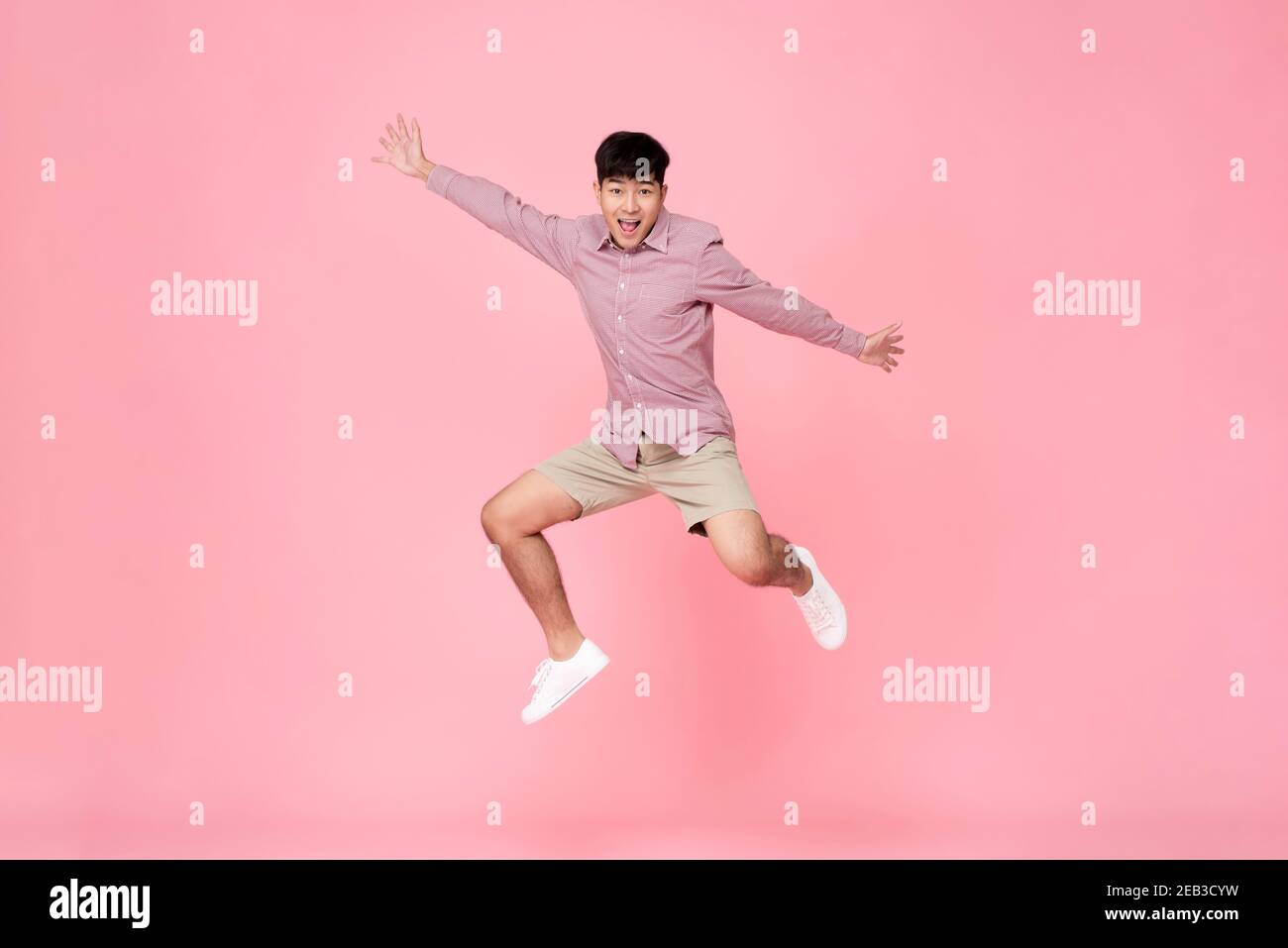 Energetic happy smiling young Asian man in casual clothes jumping studio shot isolated in colorful pink background Stock Photo
