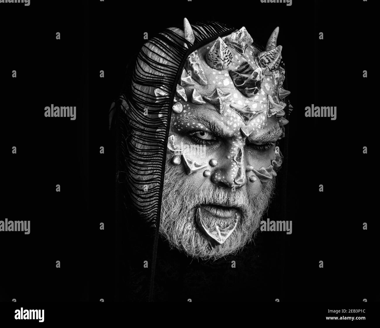 Devil man with fictional makeup. Demon with scarf on head isolated on black. Monster with white eyes and thorns on face. Alien with dragon skin and Stock Photo