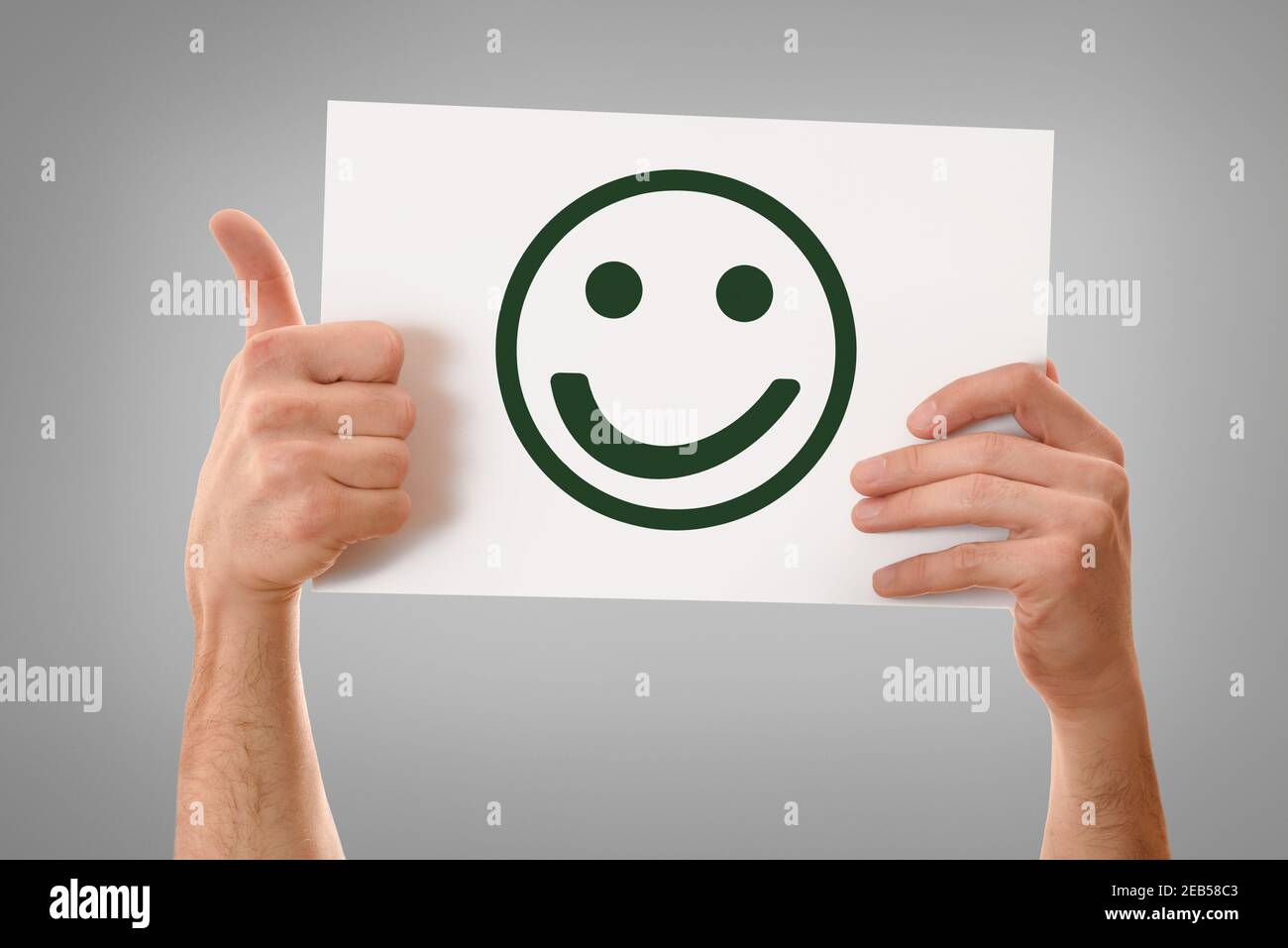 Two hands holding white sheet horizontally with happy face emoticon with finger with ok gesture and isolated gray gradient background Stock Photo