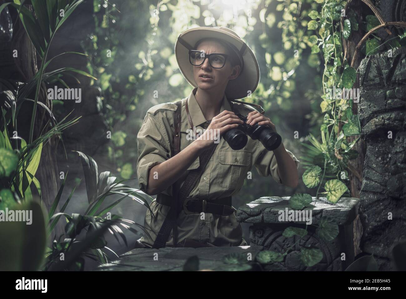 Brave woman exploring the tropical jungle and finding ancient ruins, she is holding binoculars and looking around Stock Photo