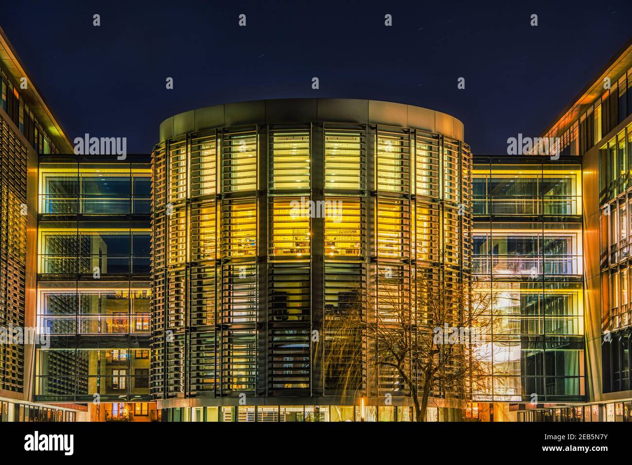 Modern opulent cylindrical office or headquarter illuminated at night with sun blinds and side passageways features a contemporary massive facade Stock Photo
