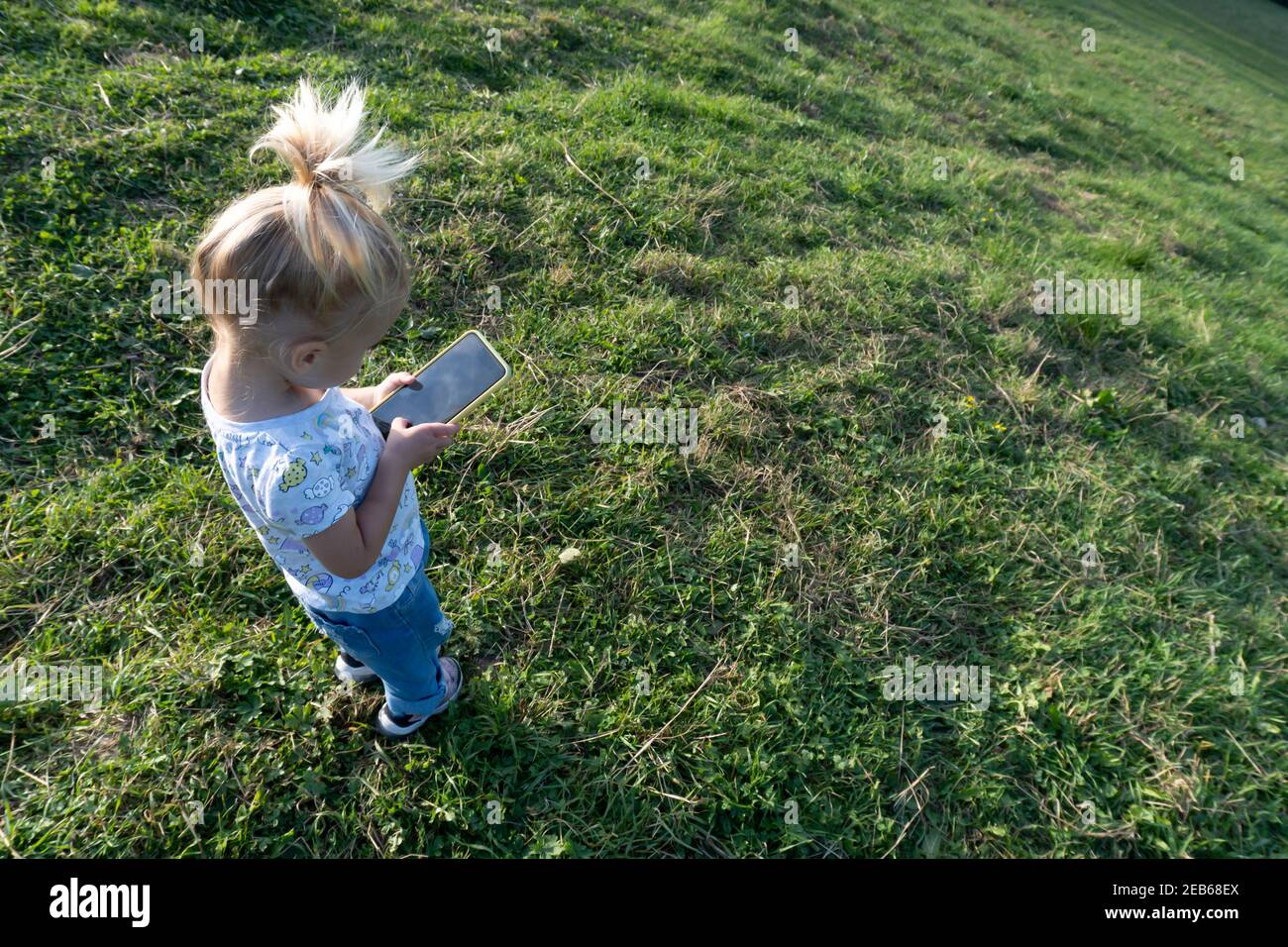 Cute caucasian blond girl playing or learning at mobile phone with black screen Stock Photo