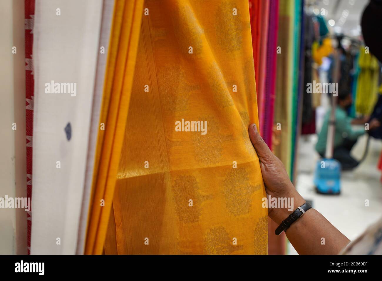 hand of a lady selecting yellow colored saree in a shop. Stock Photo