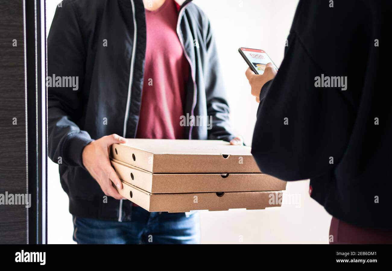 Pizza delivery to home door after online order with mobile phone. Deliverer holding fast food boxes and customer using smartphone app to pay or tip. Stock Photo