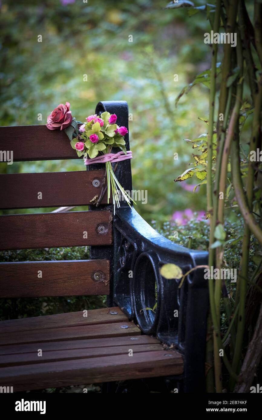 A bouquet of plastic artificial roses tied to a bench in a garden. Stock Photo