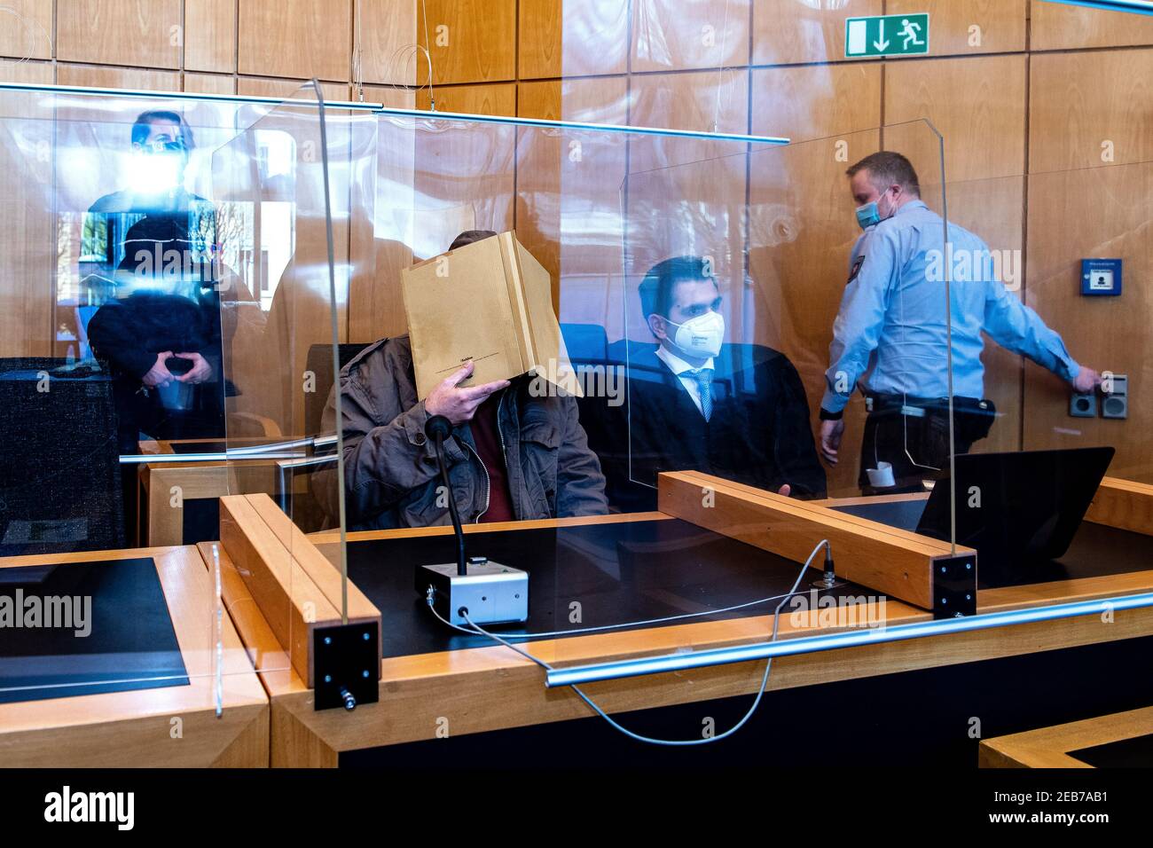 12 February 2021, North Rhine-Westphalia, Münster: The 50-year-old defendant (M) from Hanover sits with a file in front of his face in the Münster abuse complex before the pronouncement of the verdict in a room at Münster Regional Court next to his lawyer Erkan Görgülü (2nd from right). He is alleged to have severely sexually abused the foster son of the 27-year-old main defendant in the fall of 2019 in an apartment at his residence. Further trials in the matter are pending at Münster Regional Court. Judgments are not expected here until the spring. Photo: Guido Kirchner/dpa Stock Photo