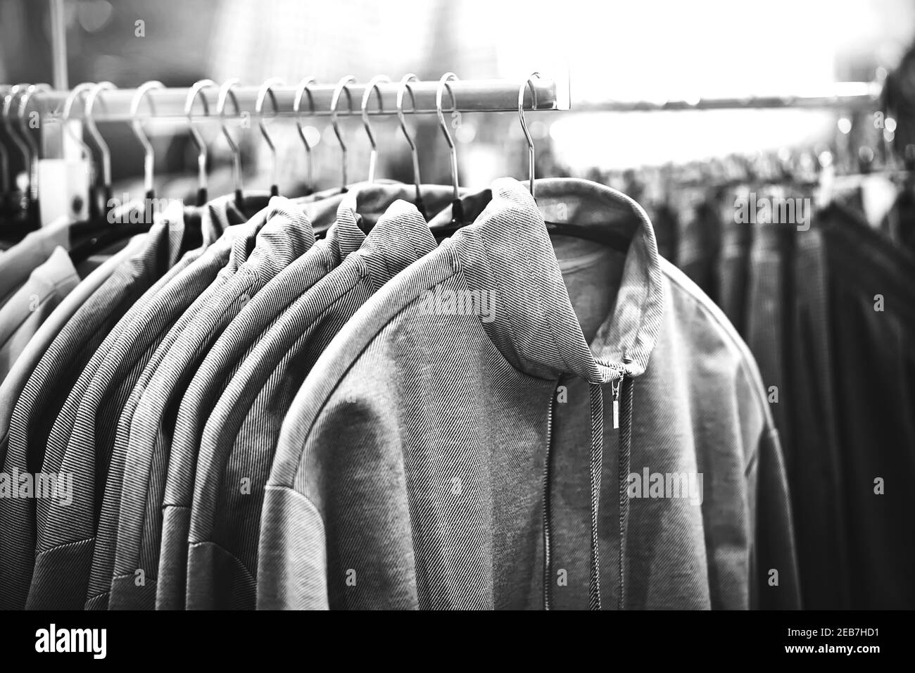A black-and-white image of hoodies hanging on hangers in a clothing store in the mall. Shopping. Stock Photo