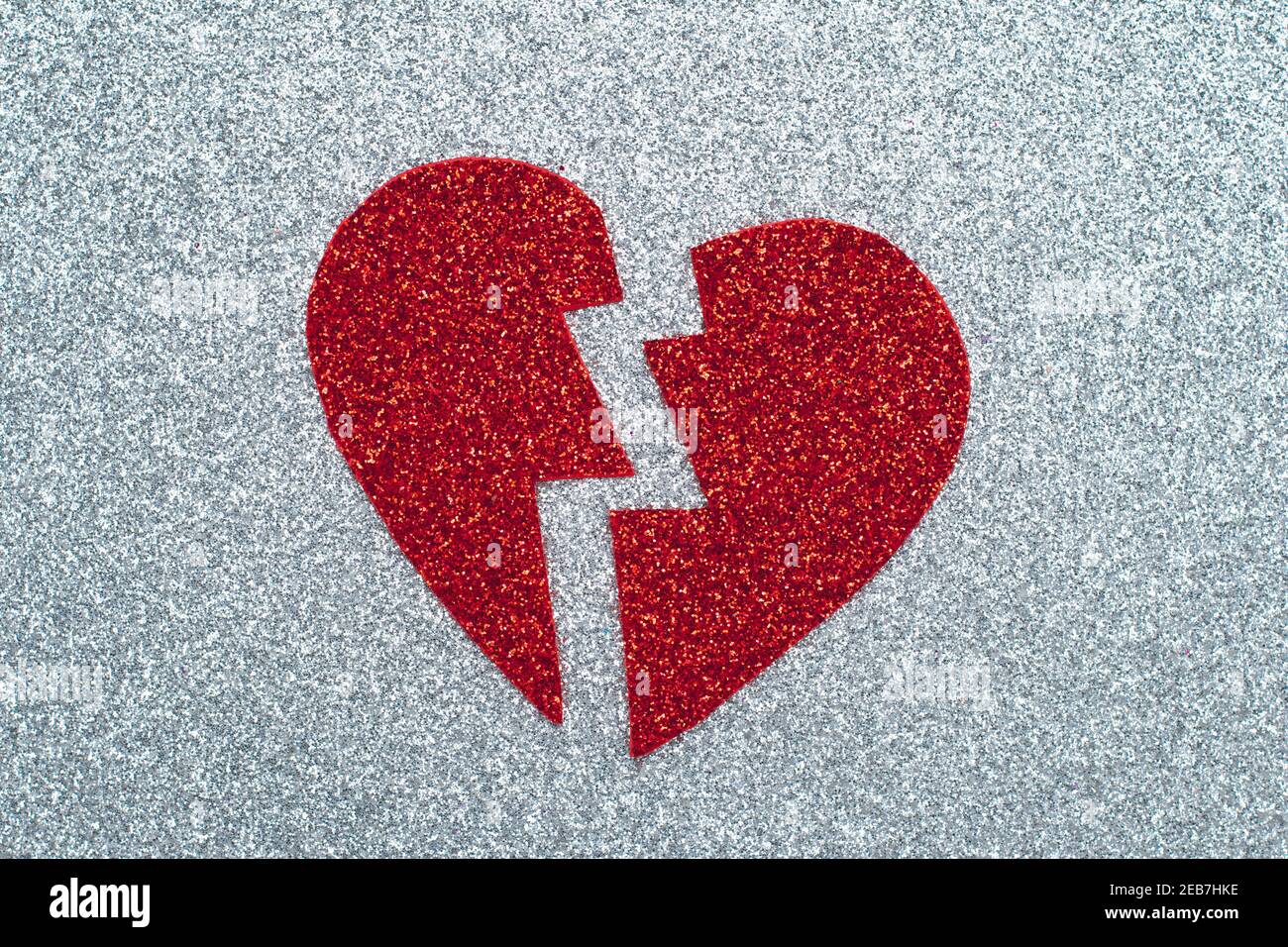 Broken red heart on gray glitter paper, a break up concept. Tinsel applique. A symbol of love, Valentine's Day, romantic feelings and emotions. Abstra Stock Photo