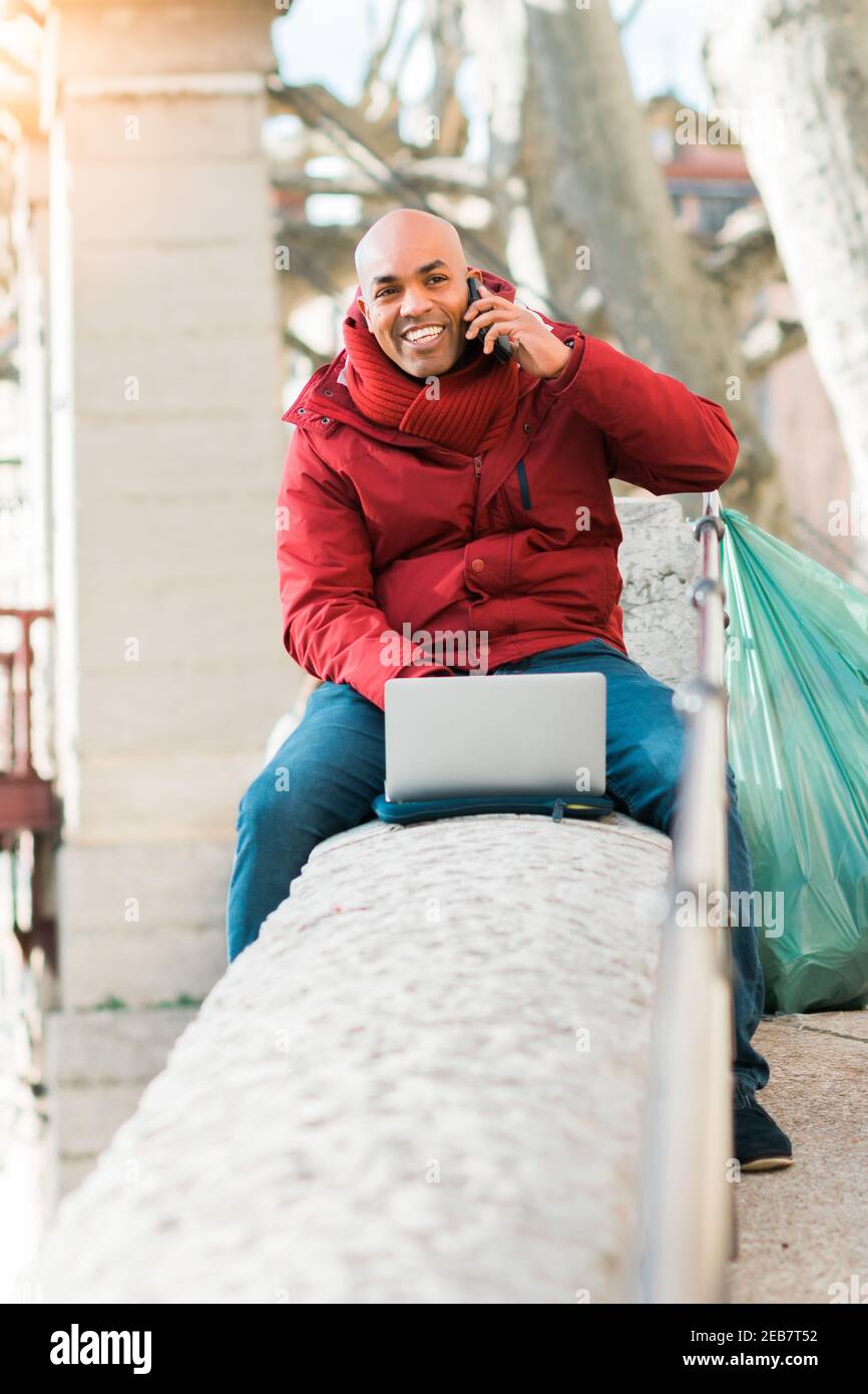 Happy smiling Hispanic male using a laptop computer while talking on the phone Stock Photo