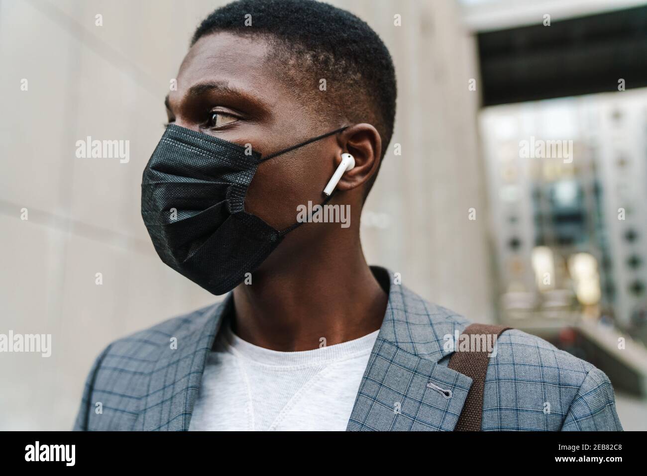 Confident african american man posing in face mask and earphones outdoors Stock Photo