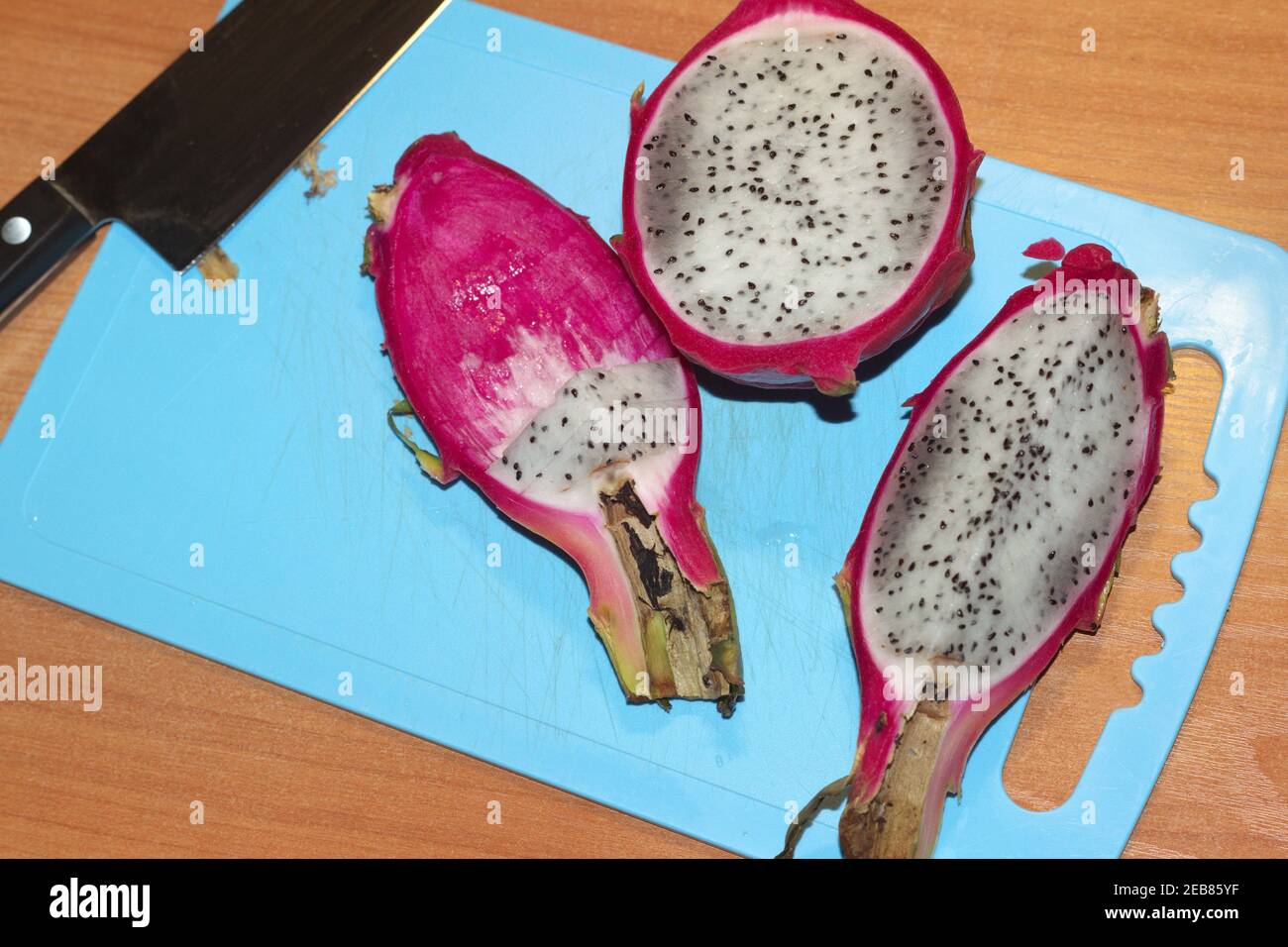 dragon fruit, sliced on a blue plastic cutting board. half, quarter, pieces of tropical exotic fruit with bright pink peel and gray pulp with small bl Stock Photo