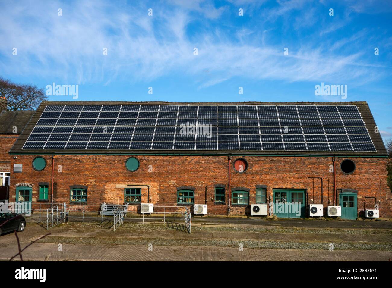 Large array of solar panels on the roof of a farm building, and air source heat pump along the wall  both using alternative green energy technology Stock Photo