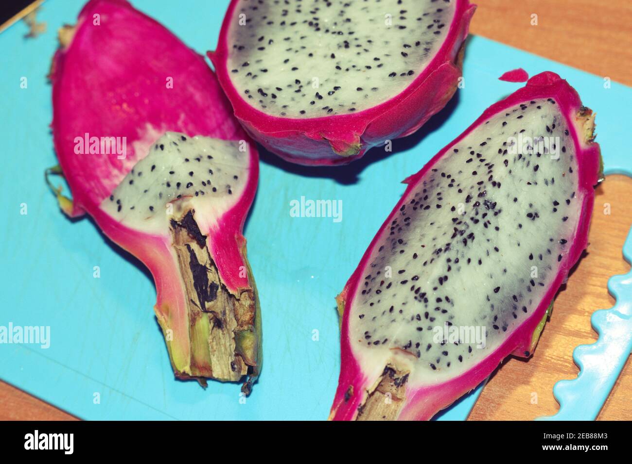 dragon fruit, sliced on blue plastic cutting board. half, quarter, pieces of tropical exotic fruit with bright pink skin and gray flesh with small bla Stock Photo
