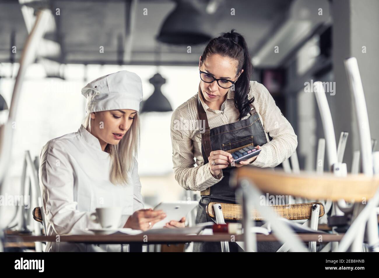 Female chef and waitress sit over bills calculating after hours in a restaurant. Stock Photo