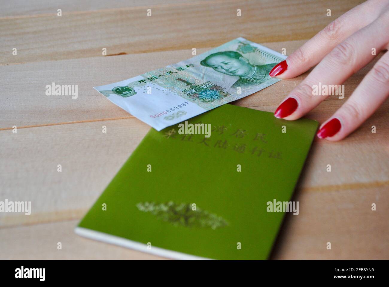 Woman fingers holding green travel document of MTP, Mainland China travel permit for Taiwan residents and 1 yuan bill with the portrait of Mao Zedong Stock Photo