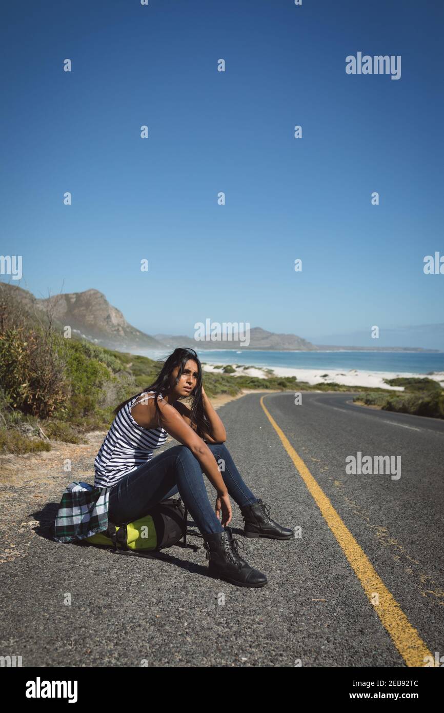 Mixed race woman sitting by the road and hitchhiking Stock Photo