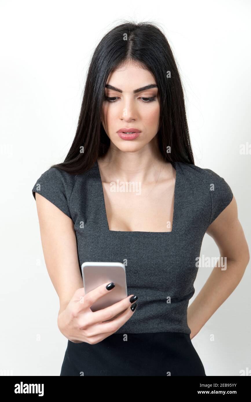 Young business woman holding her mobile phone with one hand. She is looking at it and looking serious. Stock Photo