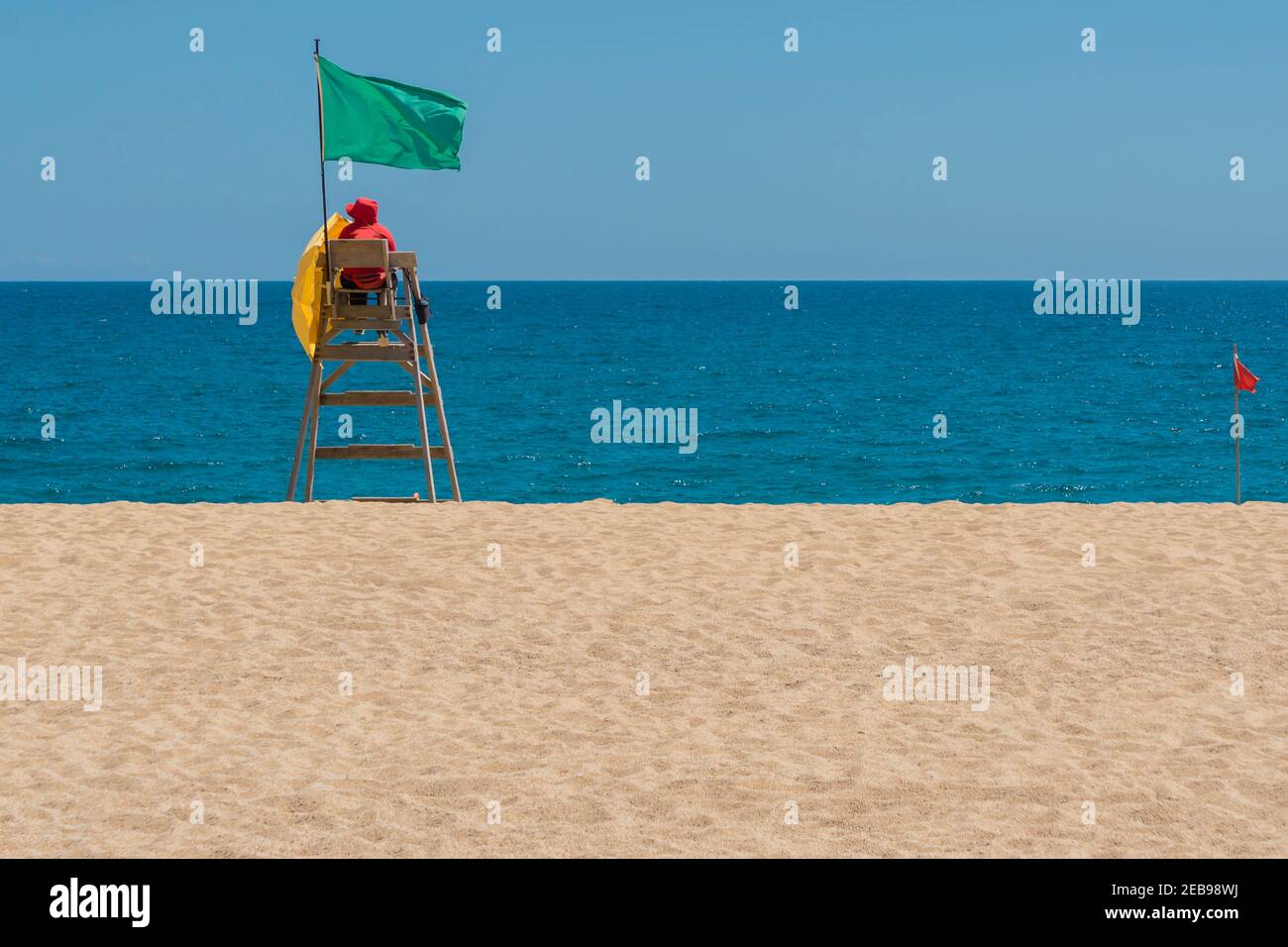 Lifeguard on rescue post at sandy beach near sea with green flag. Lifeguard searching sea areal. Safe vacation concept. Clean endless beaches. Copy sp Stock Photo